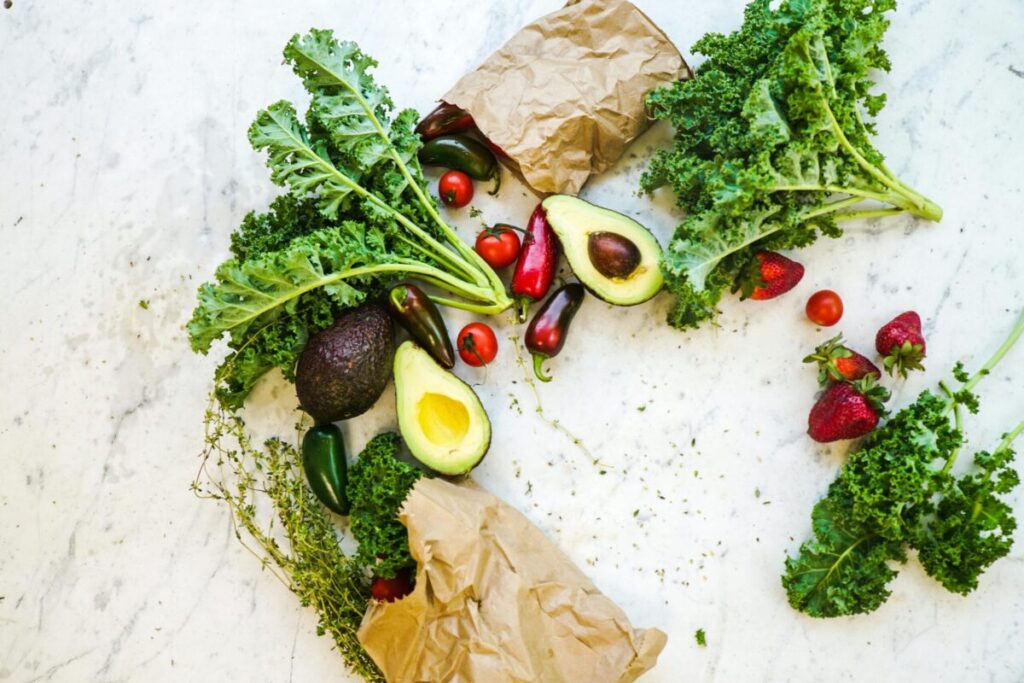 Avocado, kale, and more fresh produce artfully arranged on a marble surface.