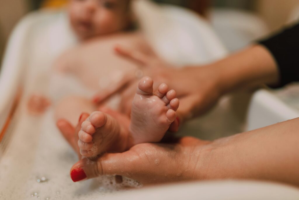 Close-up of a baby's feet during a bath, with an adult's hands gently holding them.