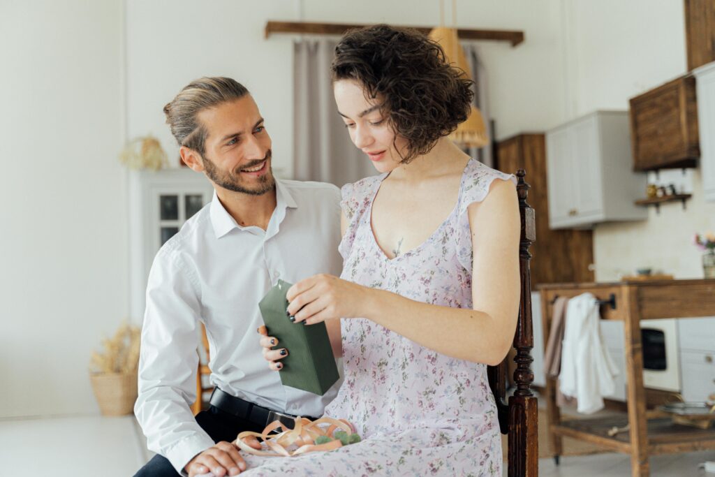 A couple sharing an intimate moment while opening a thoughtful gift together indoors.