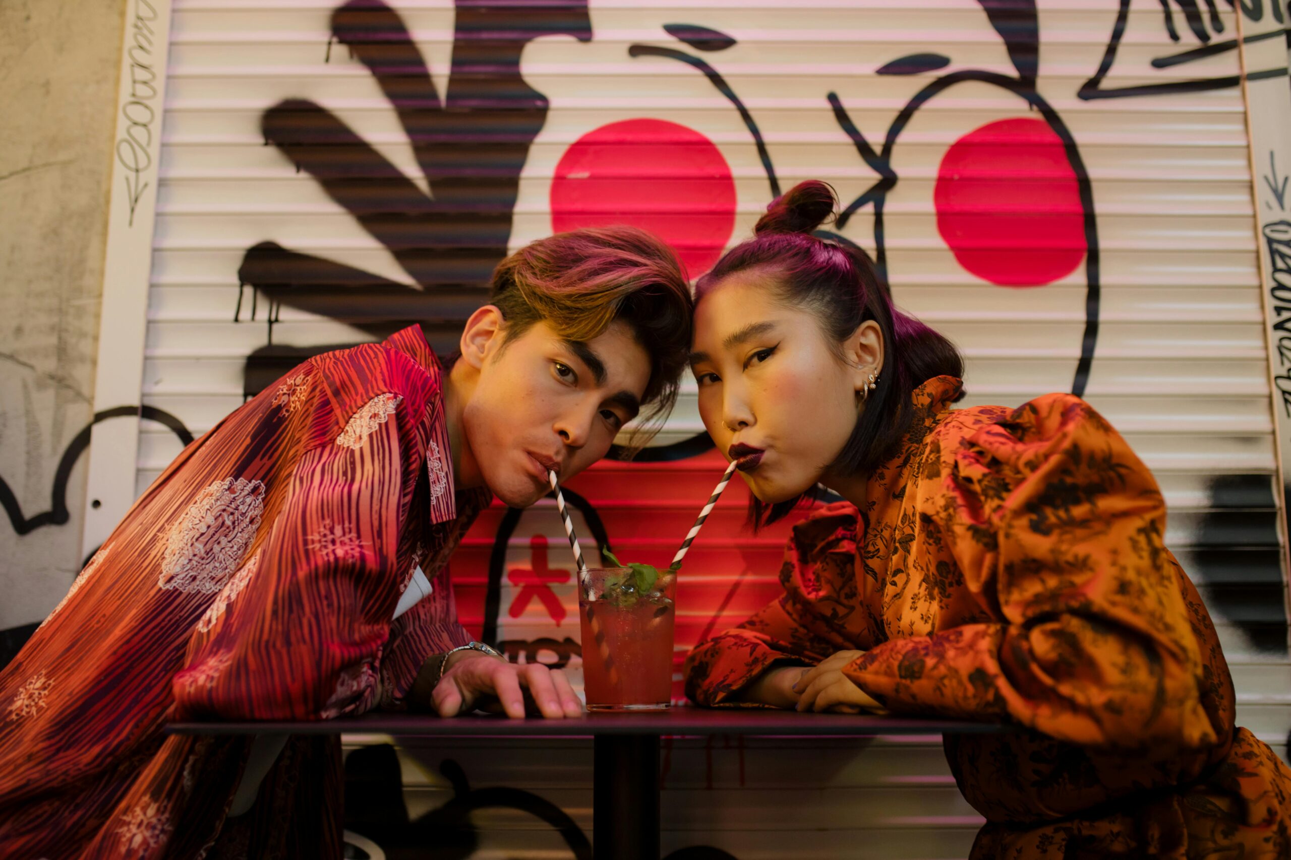 Couple sharing a trendy drink in a graffiti-decorated urban café setting. Modern fashion vibe.