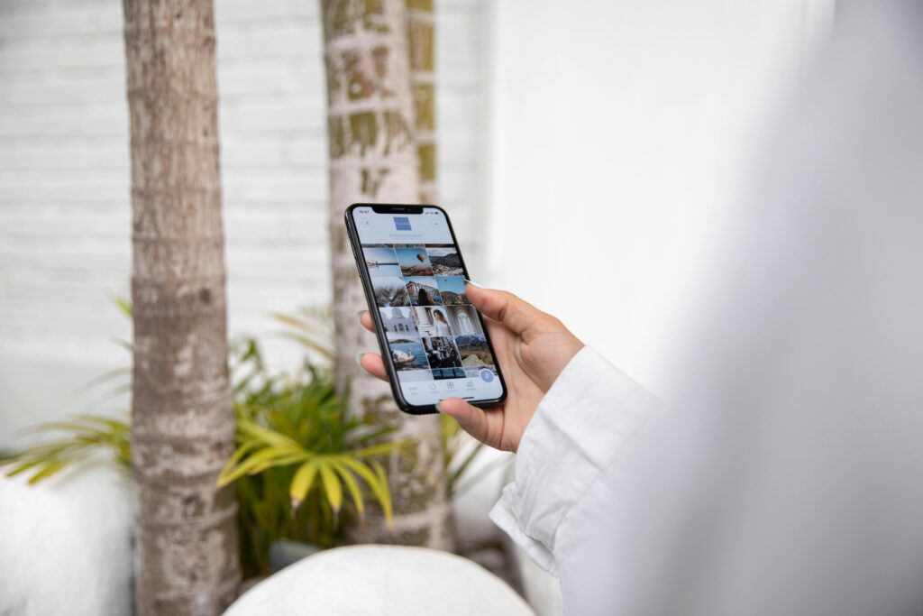 A woman using a smartphone to browse social media while standing outdoors in a tropical setting.