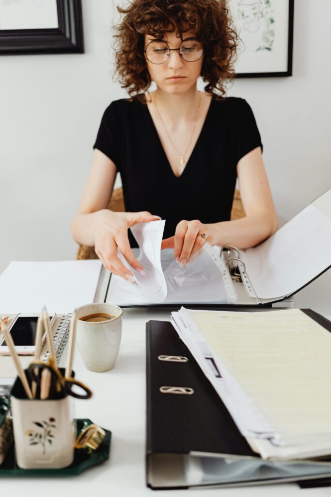 Caucasian woman with curly hair sorting documents at a desk in a contemporary workspace.