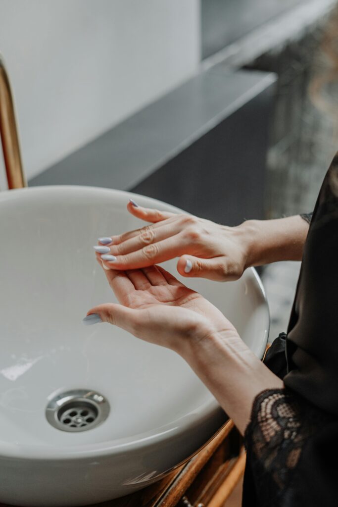 Close-up of woman applying cream on hands beside a stylish bathroom sink.