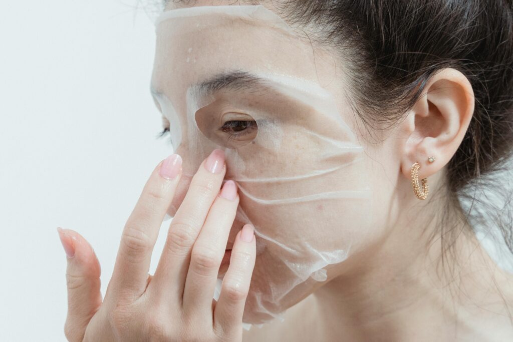 Asian woman applying a hydrating sheet mask for skincare routine.