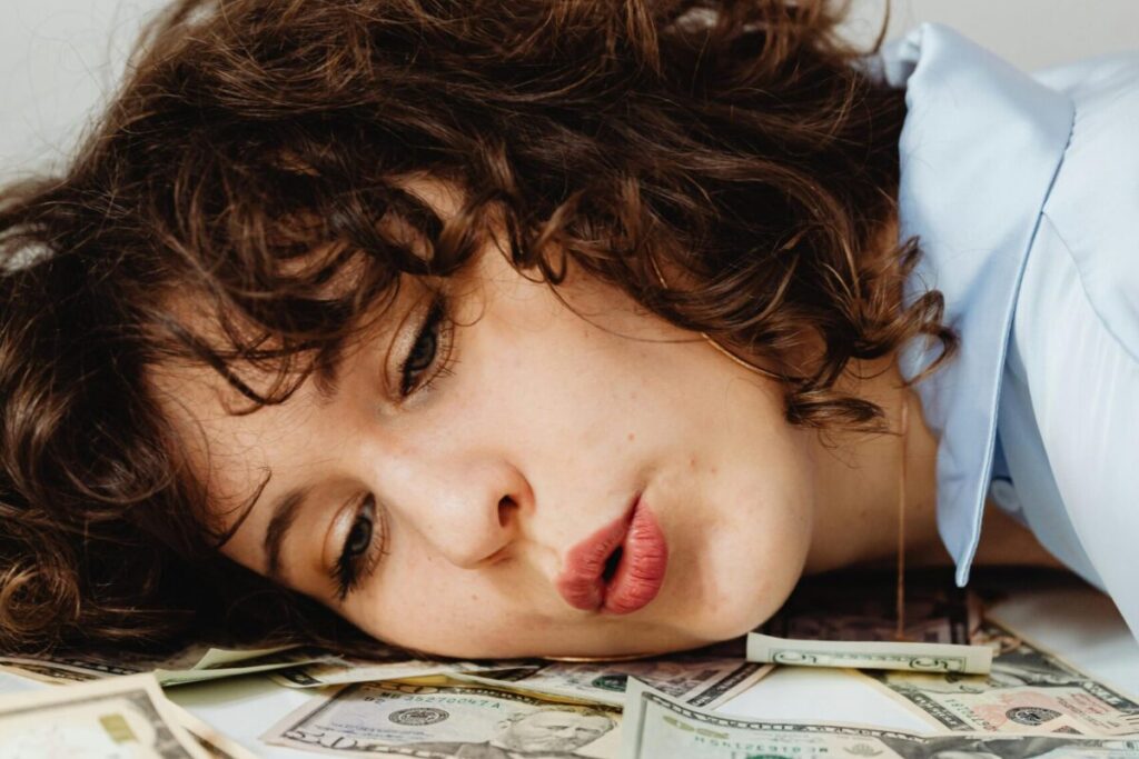 Close-up of a curly-haired woman resting on US dollar bills, conveying financial contemplation.