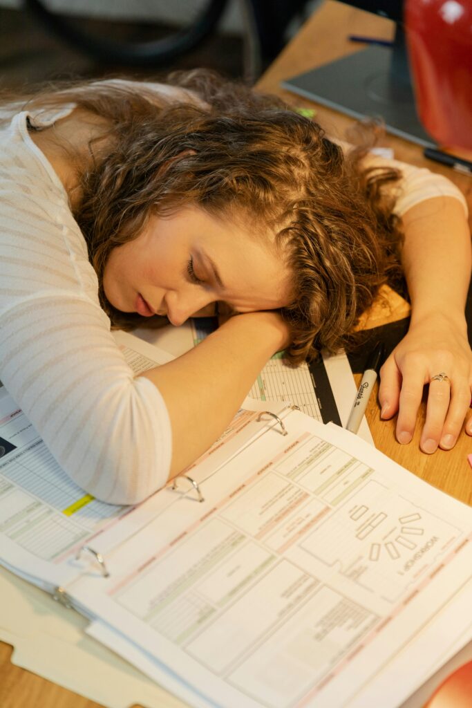 Tired female employee sleeping on desk surrounded by documents and office supplies.