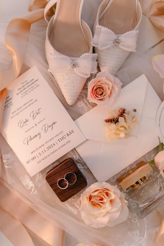 Chic wedding flat lay featuring invitations, shoes, roses, and rings for a sophisticated bridal theme.