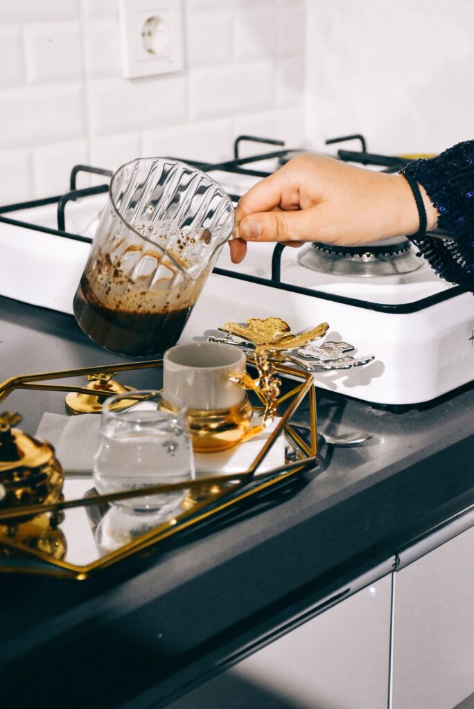 A woman carefully pours coffee from a glass pot on a stylish tray in a modern kitchen.