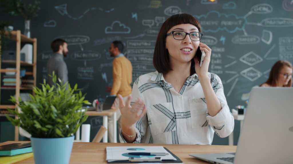 Young woman on phone in a creative office, brainstorming on chalkboard.